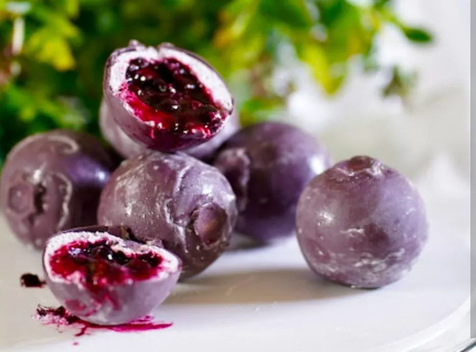 A pile of blueberry-shaped entremets with two cut open, revealing dark berry compote inside